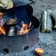 Close-up of a metal campsite fire ring with burning wood and stacked firewood — useful detail image of on-site fire facilities/amenities. Source page: Rates (https://www.rockyvalleyresort.com/rates).