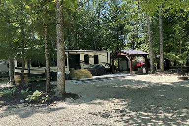 Shows an RV parked in a wooded, gravel campsite with site amenities (picnic area, shelter) — useful depiction of RV accommodations from the site gallery/home content.