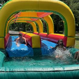Inflatable water/slip-and-slide feature with participants in a grassy setting — highlights seasonal water activity offered at the campground (Gallery page).