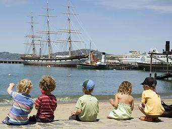 Five young children sit on the beach on a July afternoon at Aquatic Park Cove, San Francisco.