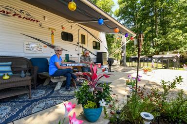 Close view of an RV campsite with awning, patio setup and landscaping — shows typical RV pitch and guest setup on the property (matches homepage/gallery context).