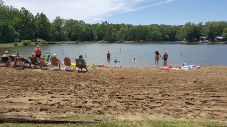 Beach and roped swimming area on the lake with people enjoying the water — highlights waterfront amenities and recreation; shown on the Home page.