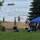 Beach and lakeshore scene with people, canopy and swimming area — demonstrates the campground’s sandy beach and recreation on Turtle Lake (from amenities/homepage).