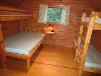 Interior of a small wood cabin showing bunk beds and a larger bed — useful for the property's cabin/lodging gallery (from the campground 'ways to stay' photos).