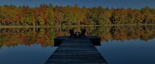 Scenic hero image with a dock extending onto a calm pond surrounded by trees — strong overview of the property’s lakeside setting (used as hero/background imagery on the site).