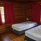 Redfeather Ranger Cabin showing two twin beds, nightstand, lamp, dresser, and two windows with red drapes. 