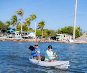 Couple kayaking off the coast of Big Pine Key in Florida with RV sites and palm trees in the background.