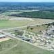 Aerial view of a rural campground with RVs and mobile homes, surrounded by open fields, trees, and a power line tower.