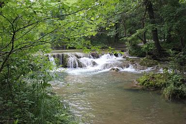 A waterfall with lush greenery surrounding it during the summer
