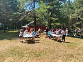 Open grassy area with people, picnic tables and a cabin/structure in the background — illustrates common area/amenity space and campsite atmosphere on the property (from Activities page).