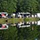 Clear photo of RVs and trailers pitched along the lake with reflections in the water — good detail of lakeside RV sites (from the main site gallery).