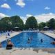 Clear daytime photograph of the campground swimming pool with deck chairs, umbrellas and building at the right — useful to show on-site pool amenity; sourced from the property homepage gallery.
