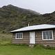 view of cabin surrounded by grass and tall cliff behind