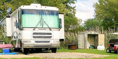 A motorhome parked near a shed and golf cart in a grassy area.