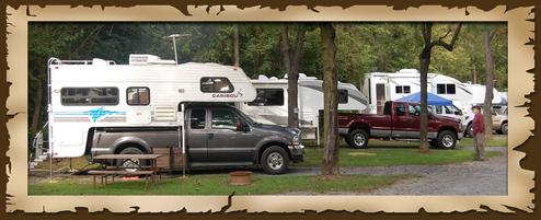 Shows multiple RVs/truck campers parked on level, wooded RV sites with picnic tables and fire rings — useful view of typical RV pitches. Comes from the homepage gallery slider for the property.