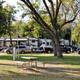 Wide campsite view showing several full-hookup RV sites, trees and picnic table in foreground — useful overview of the resort grounds and site spacing (gallery page).