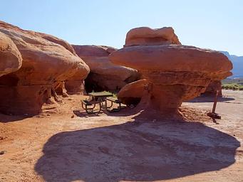 A picnic table underneath unique, overhanging red rock features. 