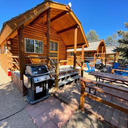 Close view of KOA-style wood cabin with porch, picnic table and grill — a clear photo of on-site cabin accommodations consistent with the campground’s ‘ways to stay’ images.
