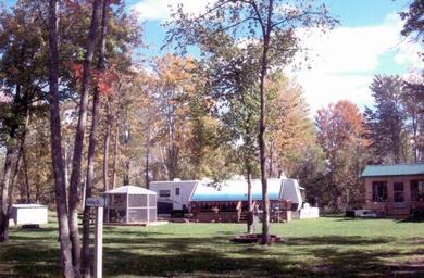 Open grassy area with trailers, building and mature trees showing campground common area and facilities; from the Whitetail Ridge Campground Photos gallery on the site.