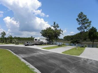 Ground-level view of paved road and pull-thru/back-in gravel pads with waterfront sites and picnic tables — useful for showing individual site setup (Site 15 / RV lodging image).