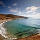 Sandy beach with ocean and small waves and steep coastal bluffs covered in grass. 