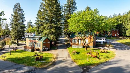 View of multiple cabin units and grassy picnic areas along paved roads — an on-property shot (ways-to-stay) that illustrates the campground's cabin lodging and site layout.
